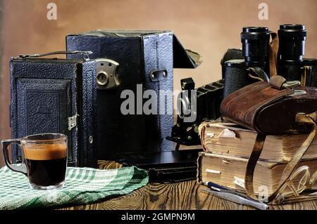 Stack of old books, binoculars, vintage camera, frayed leather cases on a wooden table Stock Photo