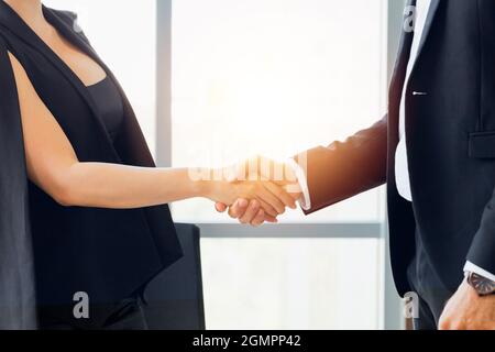 Close-up of businessman shaking hands together with business woman in indoor office environment - business greeting, success, teamwork concept Stock Photo