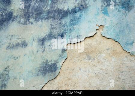 Wall of old building with partially fallen off plaster in gray and blue colors. Space is divided into two parts of different structures. Stock Photo