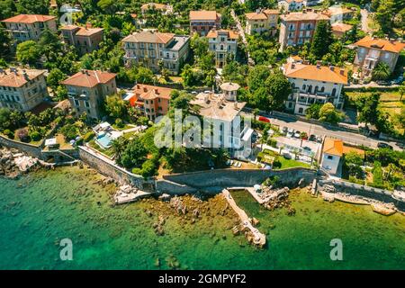 Beautiful villas near the coast of rocky beach in a small town Lovran, Croatia. Arial view of Lungomare sea walkway with transparent water. Stock Photo