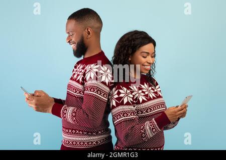 People and technology concept. Happy black couple holding smartphones and standing back to back, blue background Stock Photo