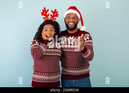 Surprised african american couple in Christmas sweaters pointing at camera over blue background Stock Photo
