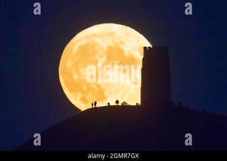 Glastonbury, Somerset, UK.  20th September 2021.  UK Weather.  The full Harvest Moon rises up into the clear night sky from behind St Michael’s Tower on Glastonbury Tor in Somerset silhouetting the people on the summit.  Picture Credit: Graham Hunt/Alamy Live News Stock Photo