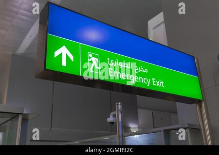 Emergency exit sign in English and Arabic glowing green at airport Stock Photo