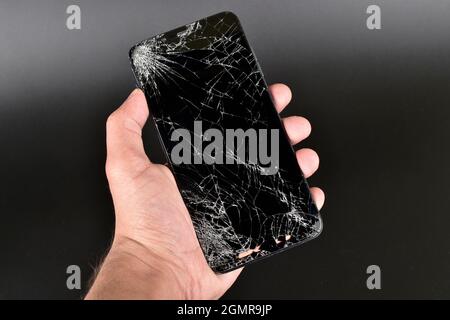 Hand Holding Broken Smartphone on Dark Background Stock Photo