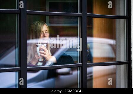 sadly depresive middle aged female looking through the window, melancholy woman in the window Stock Photo