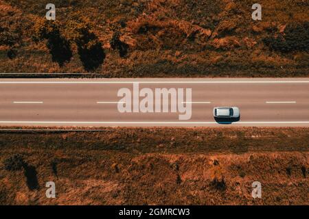 Aerial shot of single gray car driving down the road through countryside in late summer, drone top down image Stock Photo