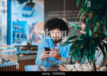 Young man dressed in stylish clothes enjoying their coffee at a cafe bar while using his mobile Stock Photo