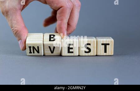 Best invest symbol. Businessman turns wooden cubes and changes the word 'invest' to 'best'. Beautiful grey background. Business and best invest concep Stock Photo