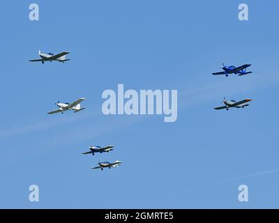 Six light aircraft fly in loose formation against a clear blue sky during an airshow display. Stock Photo