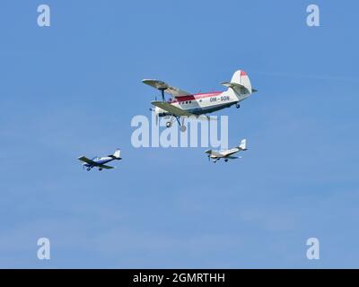 Vintage biplane flying with two small aircraft in formation during an airshow against a clear blue sky. Stock Photo