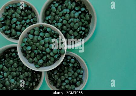 Spirulina algae tablets. Spirulina pills in cups on a green background. Vegetarian omega three.Super food Stock Photo