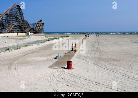 People walking on a wooden path on the beach in Wildwood, NJ with the Roller Coaster in the background Stock Photo