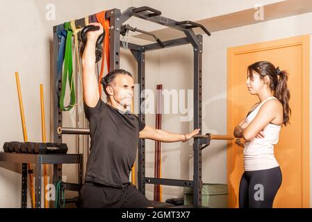 Man doing shoulder press exercises with kettlebell while woman look at him. Stock Photo
