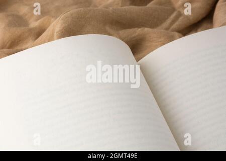 opened blank book on a light brown fabric background, closeup paperback mockup template with copy space Stock Photo