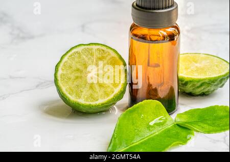 Beautiful packshot of Bergamot essential oil in a small brown glass bottle with fresh bergamot fruit with green leaf on the marble tabletop, wet of wa Stock Photo