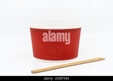 Front view a takeaway noodle bowl container with wooden chopsticks, empty takeaway red food container on white background, blank space for branding. Stock Photo