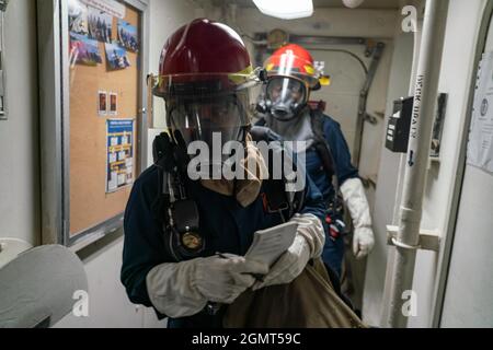 PACIFIC OCEAN (September 9, 2021) Operations Specialist 3rd Class Jorge Nunez, front, Santa Ana, Calif., and Operations Specialist 2nd Class Terrica Scarlett, from Brooklyn, N.Y., investigate a simulated fire during a general quarters drill onboard amphibious dock landing ship USS Pearl Harbor (LSD 52), Sept 9. Pearl Harbor, part of the USS Essex Amphibious Ready Group (ARG), along with the 11th Marine Expeditionary Unit (MEU), is operating in the U.S. 7th Fleet area of responsibility to enhance interoperability with allies and partners and serve as a ready response force to defend peace and s Stock Photo