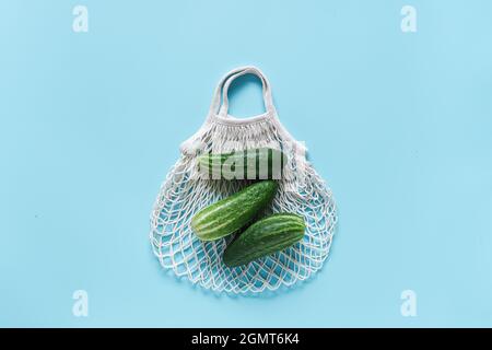 Fresh green cucumbers vegetables on reusable shopping eco-frendly mesh bag on blue background. Concept no plastic and zero waste. Copy space Top view Stock Photo