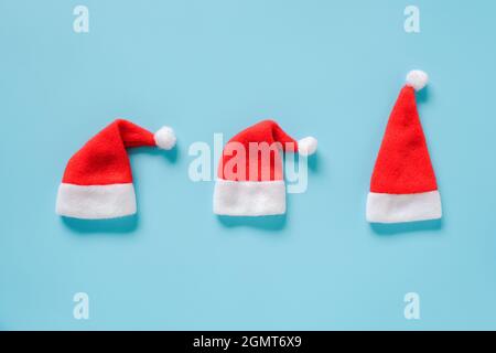 Winter holiday composition. Three red Santa Claus Hats on blue background. Greeting card Layout Top view Flat lay Template for design, card, invitatio Stock Photo