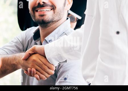 Close-up of two businessmen shaking hands together in indoor office environment - business greeting, success, teamwork concept Stock Photo