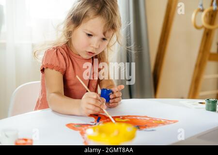 Young girl spending a time drawing using online lessons on laptop at home. Distance learning, online education. Stock Photo