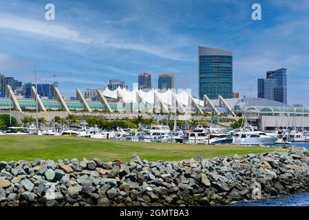 View of futuristic modern complex of the San Diego Convention Center on the waterfront with boats docked at Marina and rocky shoreline, San Diego, CA Stock Photo
