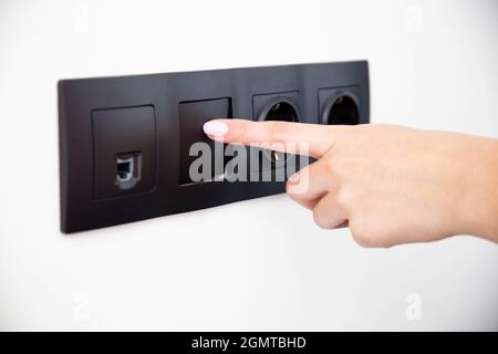 The girl presses the button of the broken electrical switch combined with the socket. Electric shock concept with faulty equipment Stock Photo