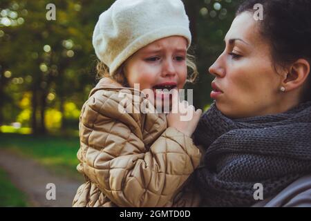 sad girl in a mustard-colored jacket hugs her mother Stock Photo