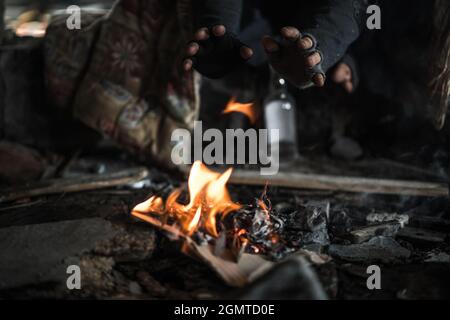 Homeless Men Heating Himself with Small Fire Inside Abandoned House Ruins. Stock Photo