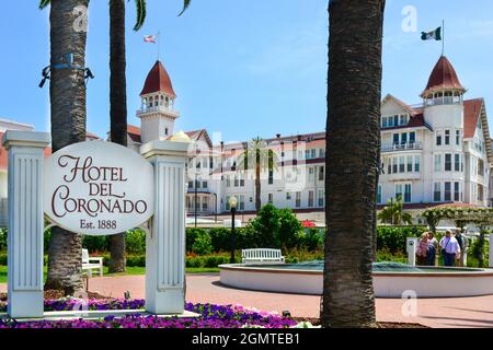 Hotel del Coronado signpost with blooming colorful flowers and palm trees with iconic Victorian property in background on Coronado Isle, San Diego, CA Stock Photo