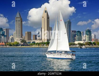 A sailboat leisurely sails in the San Diego Harbor by the Manchester Grand Hyatt Bayside Hotel as part of the stunning cityscape of San Diego, CA Stock Photo