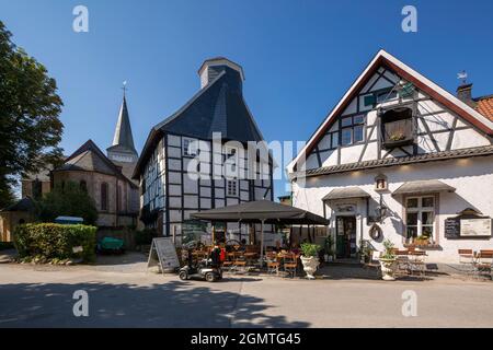 Germany, Wuelfrath, Wuelfrath-Duessel, Bergisches Land, Niederbergisches Land, Niederberg, Rhineland, North Rhine-Westphalia, NRW, Dorfstrasse in the Duessel village, f.l.t.r. catholic church Saint Maximin, half-timbered house Eyser, former sextons house and school, house 'Am Iser' with Kutscherstuben restaurant and cafe Stock Photo