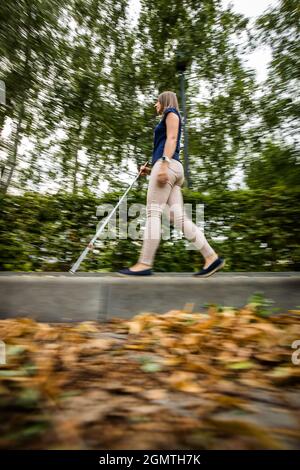 Blind woman walking on city streets, using her white cane Stock Photo