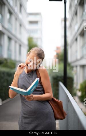 Busy personal assistant calling on the phone and taking notes at the same time while walking on the city street Stock Photo