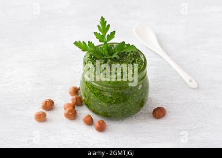 Fresh homemade parsley pesto with hazelnuts in glass jar on light gray background. delicious vegan food Stock Photo