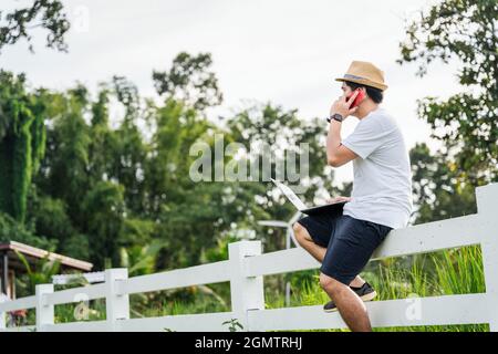 Asian young man traveler using laptop computer while enjoying beautiful tropical in nature. Freelancer guy working on freelance on netbook during vaca Stock Photo