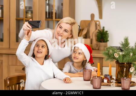 Christmas online family congratulations. Smiling european blonde mother and daughter using mobile tablet for video call friends and parents. Stock Photo