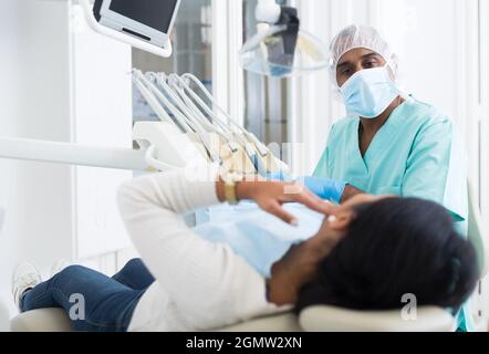 Focused hispanic dentist attentively listening to female patient toothache complains in dental office Stock Photo