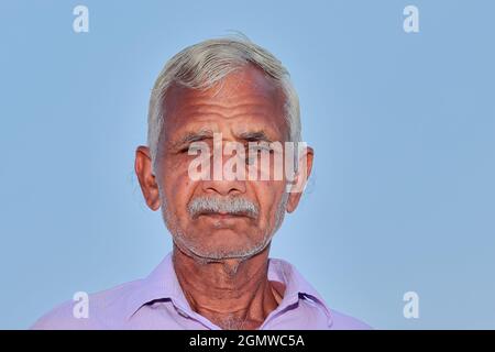 low angle shot of Close up face photo of elderly Indian Hindu farmer man with clear blue sky background behind Stock Photo