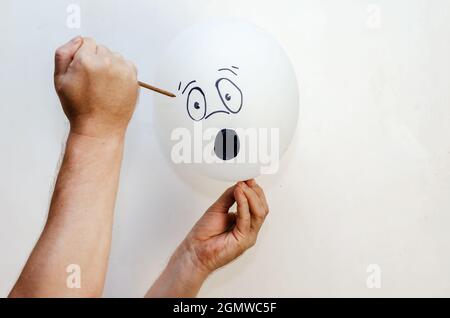A balloon with a face painted on it and a rusty nail. Man holdin Stock Photo