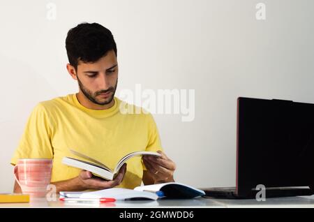 Young handsome man reading book and making notes at work desk in free time from working at home. preparing for entrance college exams, studying readin Stock Photo