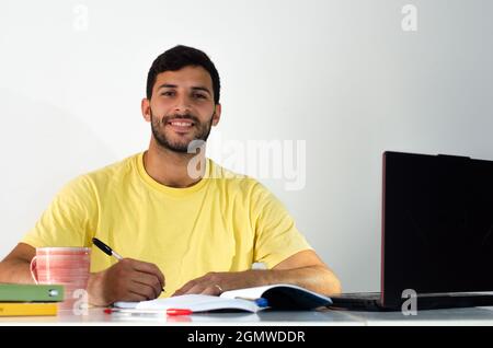 Portrait of focused student preparing for exam at home. adult student taking notes in his or her book while watching a virtual class. Businessman writ Stock Photo
