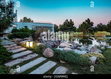 Decorative pond with artificial waterfall in courtyard of country house at summer sunset Stock Photo