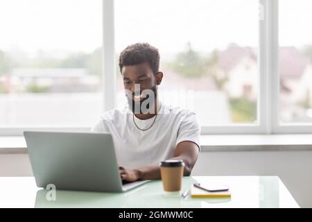 Focused concentrated young african businessman sit at desk look at laptop at office desk Stock Photo