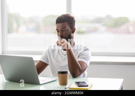 Focused concentrated young african businessman sit at desk look at laptop at office desk Stock Photo