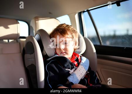 sleepy three year old boy sitting in car safety seat going to school in the morning Stock Photo