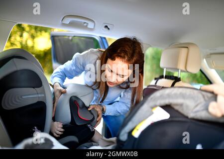 millennial mother hanging a safety cushion on a child's safety seat in a car Stock Photo