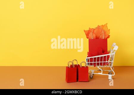 autumn shopping grocery cart with paper bags and red falling leaves on yellow background. Concept Autumn sale. copy space Stock Photo