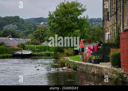Lady feeding water birds from house garden (old Victorian textile mill) & moored narrowboat - on banks of scenic Leeds Liverpool Canal, England, UK. Stock Photo